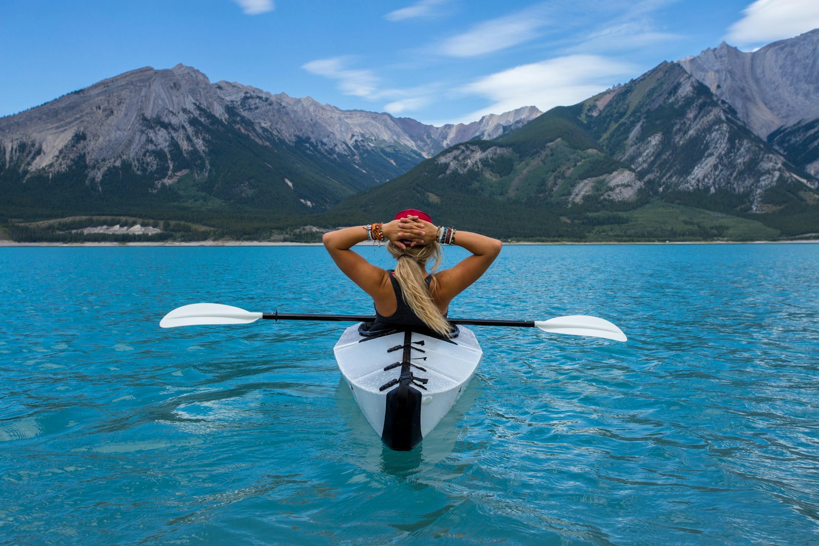 paddler in a white kayak stretching on turquoise lake water below mountains - Rivara Kayak - paddle sports gear for dealers